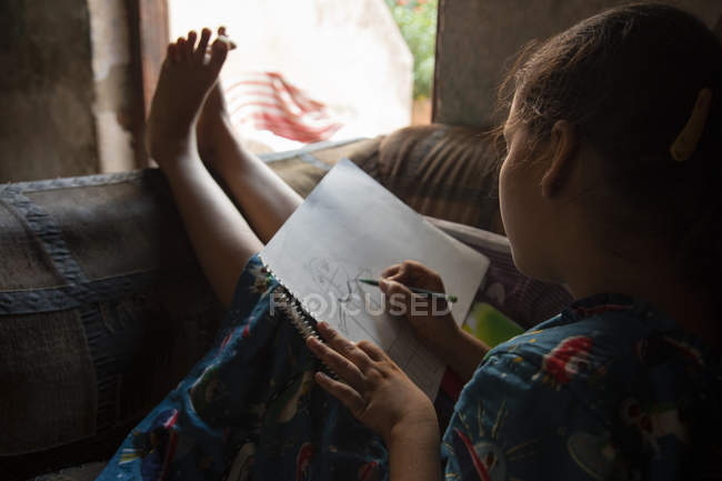 Mädchen sitzt auf dem Sofa und zeichnet auf einem Papier — Stockfoto