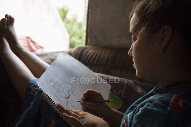 Chica sentada en el sofá y dibujando en un papel - foto de stock