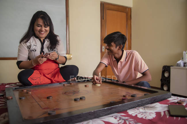 Son playing carrom-board with his mother at home. — Stock Photo