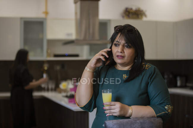 Mulher assistindo a uma chamada na cozinha com bebida na mão . — Fotografia de Stock
