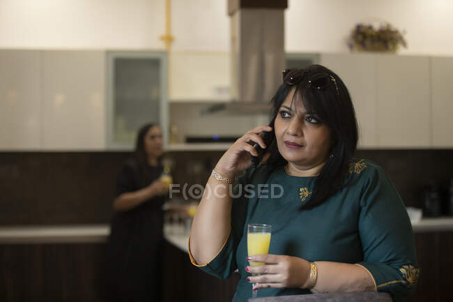 Woman attending a call in Kitchen with drink in her hand. — Stock Photo