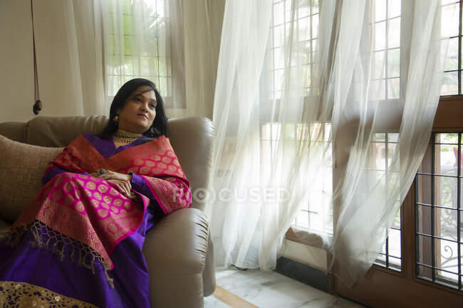 A well dressed woman sitting comfortably on a couch at her home. — Stock Photo