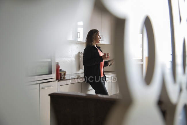 Frau trinkt Kaffee, während sie sich zu Hause in der Küche in ihren Gedanken verliert. — Stockfoto