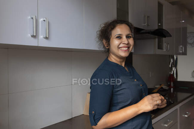 Jovem mulher de pé na cozinha e sorrindo em casa . — Fotografia de Stock