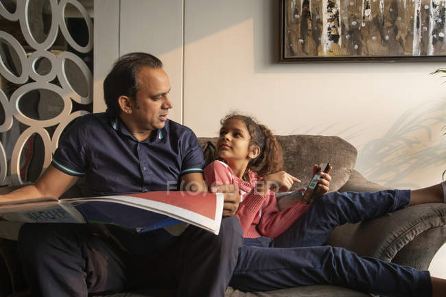 Junges Mädchen bittet ihren Vater um Hilfe, während er zu Hause die Zeitung liest. — Stockfoto