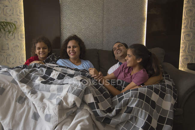 Familia feliz cómodamente sentado en el sofá debajo de una manta en casa . - foto de stock