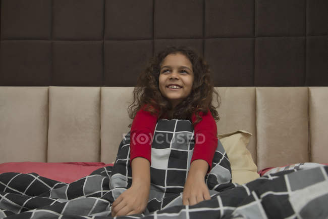 Молода дівчина сидить на ліжку половина всередині ковдри сміється . — стокове фото
