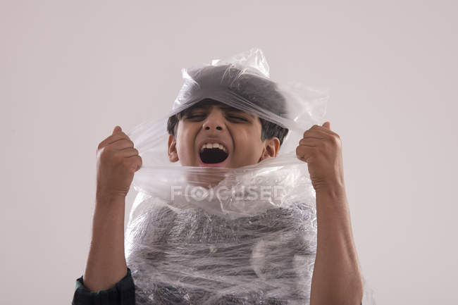 Jeune garçon enveloppé de plastique, luttant pour déchirer l'air frais . — Photo de stock