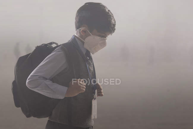 Un jeune garçon qui va à l'école avec un masque anti-pollution . — Photo de stock