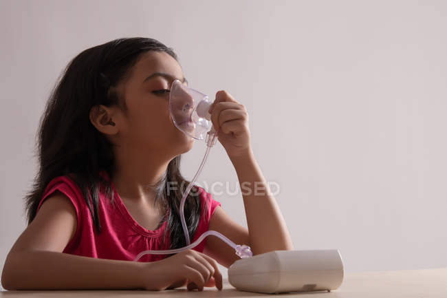 Menina sentada e inalando através de um nebulizador em casa . — Fotografia de Stock