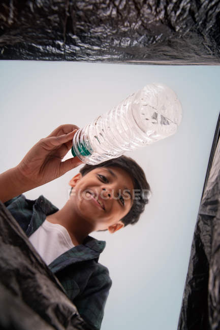 Jeune garçon jetant des déchets dans un sac poubelle . — Photo de stock