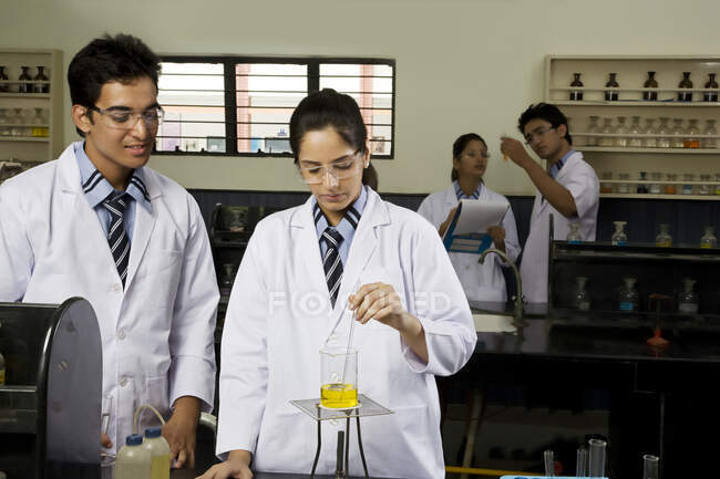 Ragazza con compagni di classe mescolando un becher con liquido giallo — Foto stock
