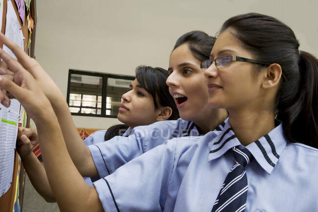 Estudiantes mirando los resultados de sus exámenes en un tablón de anuncios - foto de stock