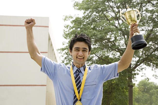 Студент с поднятыми руками и трофеями торжествует во дворе школы — стоковое фото