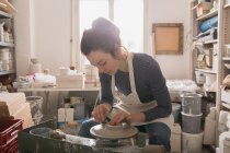 Mujer caucásica está dando forma a la cerámica de arcilla en una rueda de cerámica en un taller de cerámica
. - foto de stock