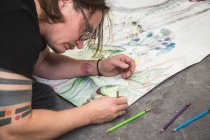 Artista masculino creativo trabajando en su taller mientras está acostado sobre papel - foto de stock