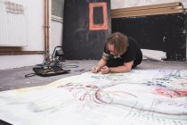Креативний художник-чоловік працює у своїй майстерні, лежачи над папером — стокове фото
