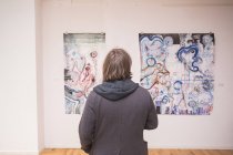 Veduta posteriore dell'artista creativo maschile che guarda la sua opera d'arte in una galleria d'arte . — Foto stock