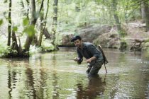 Пациент в вадере ловит рыбу на реке в лесу . — стоковое фото