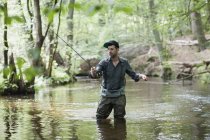 Un hombre paciente en vadeadores es la pesca con mosca en el río en la zona forestal
. - foto de stock