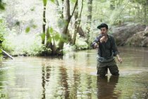 Um homem paciente em waders é pesca com mosca no rio na área florestal . — Fotografia de Stock