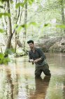 Ein geduldiger Mann in Watstiefeln fischt auf Fluss in Waldgebiet. — Stockfoto