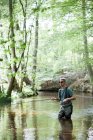 Um homem em waders é pesca com mosca no rio na área da floresta . — Fotografia de Stock