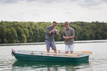 Two caucasian men are preparing their equipment for fly fishing from a boat on lake. — Stock Photo