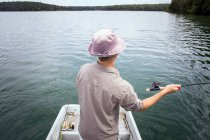 Rear view of man is fly fishing from boat on a lake. — Stock Photo