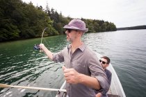 Un hombre está remando un bote de remos mientras su amigo está pescando con mosca desde un barco en el lago . - foto de stock