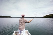 Um homem é pesca com mosca de um barco no lago . — Fotografia de Stock