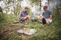 Matériel de pêche à la mouche dans l'herbe tandis que deux pêcheurs à la mouche font un barbecue dans la nature sauvage . — Photo de stock