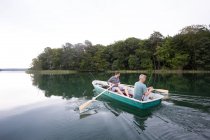 Ein Mann rudert mit einem Ruderboot, während sein Freund von einem Boot auf dem See aus fischt. — Stockfoto