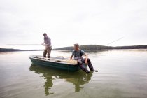 Two men in waders are fly fishing from a boat in a lake. — Stock Photo