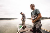 Dos hombres están poniendo en vadeadores antes de la pesca con mosca de un lago . - foto de stock