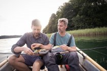 Deux hommes ramassent une mouche de pêche d'un attirail de pêche à la mouche en bateau sur la rivière . — Photo de stock
