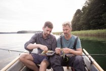 Dois homens estão escolhendo uma mosca da pesca de uma mosca que pesca o tackle no barco no rio . — Fotografia de Stock