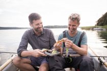 Dois homens estão escolhendo uma mosca da pesca de uma mosca que pesca o tackle no barco no rio . — Fotografia de Stock