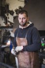 A blacksmith in a leather apron is using a cutting torch in his workshop. — Stock Photo