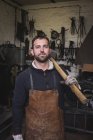 A blacksmith in a leather apron and with a sledgehammer is portrayed in his workshop. — Stock Photo