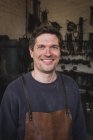 Un forgeron souriant porte un tablier en cuir et est représenté dans son atelier
. — Photo de stock