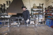 Un forgeron souriant porte un équipement de sécurité et est sur le point de souder une construction métallique dans un atelier de forgeron . — Photo de stock