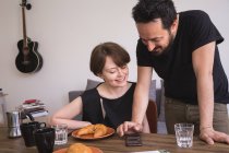 Молода пара кусає соціальні медіа на смартфоні за столом сніданку . — стокове фото