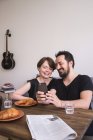 Um jovem casal está fazendo selfies com um telefone inteligente na mesa de café da manhã . — Fotografia de Stock