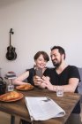 Una pareja joven está haciendo selfies con un teléfono inteligente en la mesa del desayuno . - foto de stock