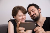 Un jeune couple fait des selfies avec un téléphone intelligent tout en se relaxant sur le canapé pendant le week-end . — Photo de stock