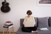 Молода жінка переглядає свій комп'ютер на дивані у вітальні . — стокове фото