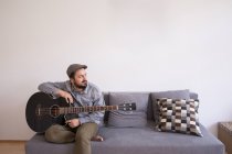 Ein junger Mann probt auf seiner Bassgitarre im Wohnzimmer. — Stockfoto