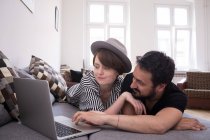A young couple is streaming TV-series on the computer while relaxing on the couch in the living room. — Stock Photo