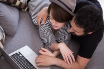 A young couple is streaming TV-series on the computer while relaxing on the couch in the living room. — Stock Photo